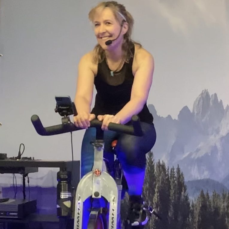 Diana auf dem Rad Frau auf einem Spinning-Bike, lächelt und spricht ins Mikrofon.